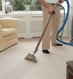 Professional carpet cleaner using a hot-water extraction wand and hose machine in a living room in Knoxville, TN.