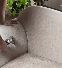 Professional upholstery cleaner deep-cleaning a fabric sofa with a handheld extraction tool and hose Knoxville, TN.