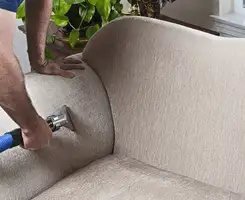 Professional upholstery cleaner deep-cleaning a fabric sofa with a handheld extraction tool and hose in Knoxville, TN.